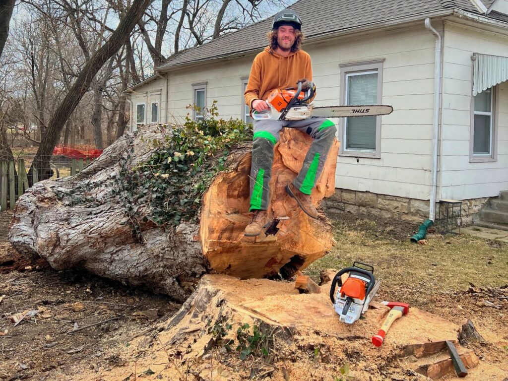 Curtis Partain, the owner of Top Tier Tree and Lawn, sitting on a tree stump with a chain saw.
