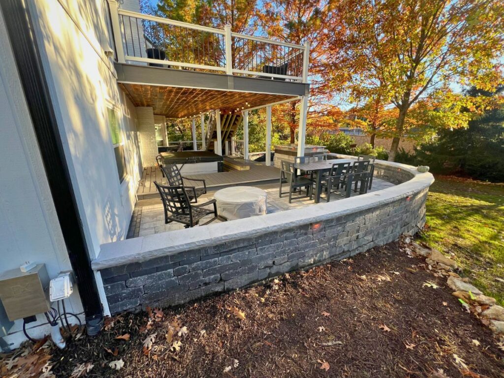 A grey brick patio in a suburban back yard surrounded by trees filled with brightly colored fall trees.