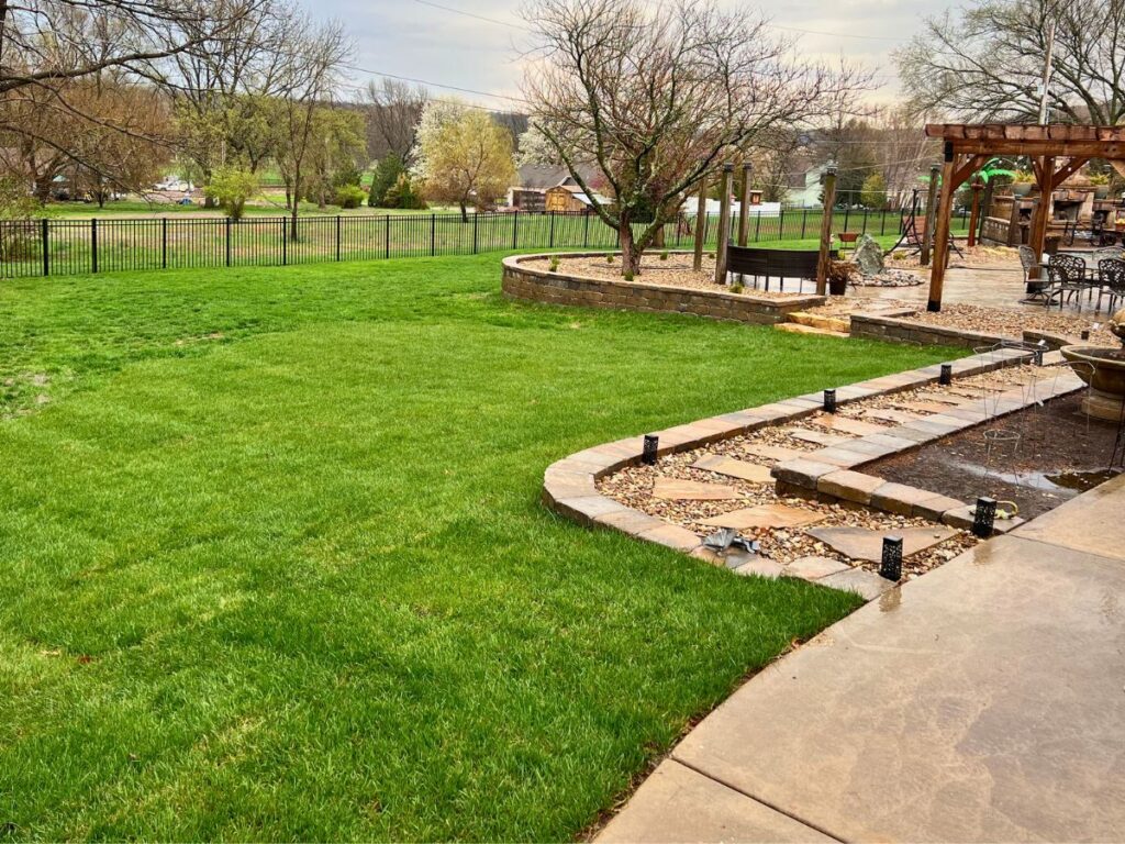 A curved walk way and stone retaining wall surrounded by green grass in a suburban back yard.