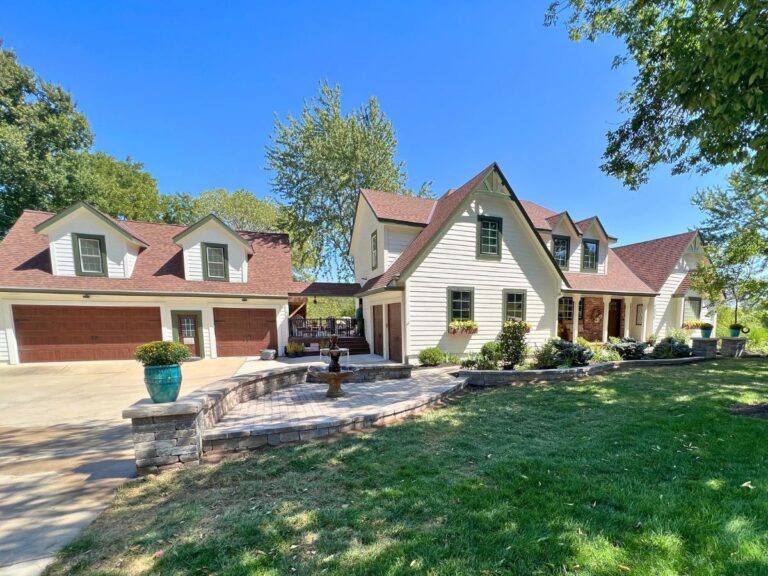 A cream-colored, two-story house with a brick patio in front.