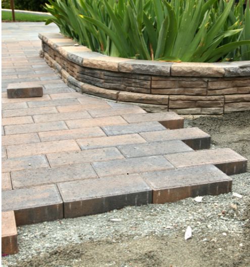 A red brick patio being constructed on a sandy foundation in a suburban back yard.